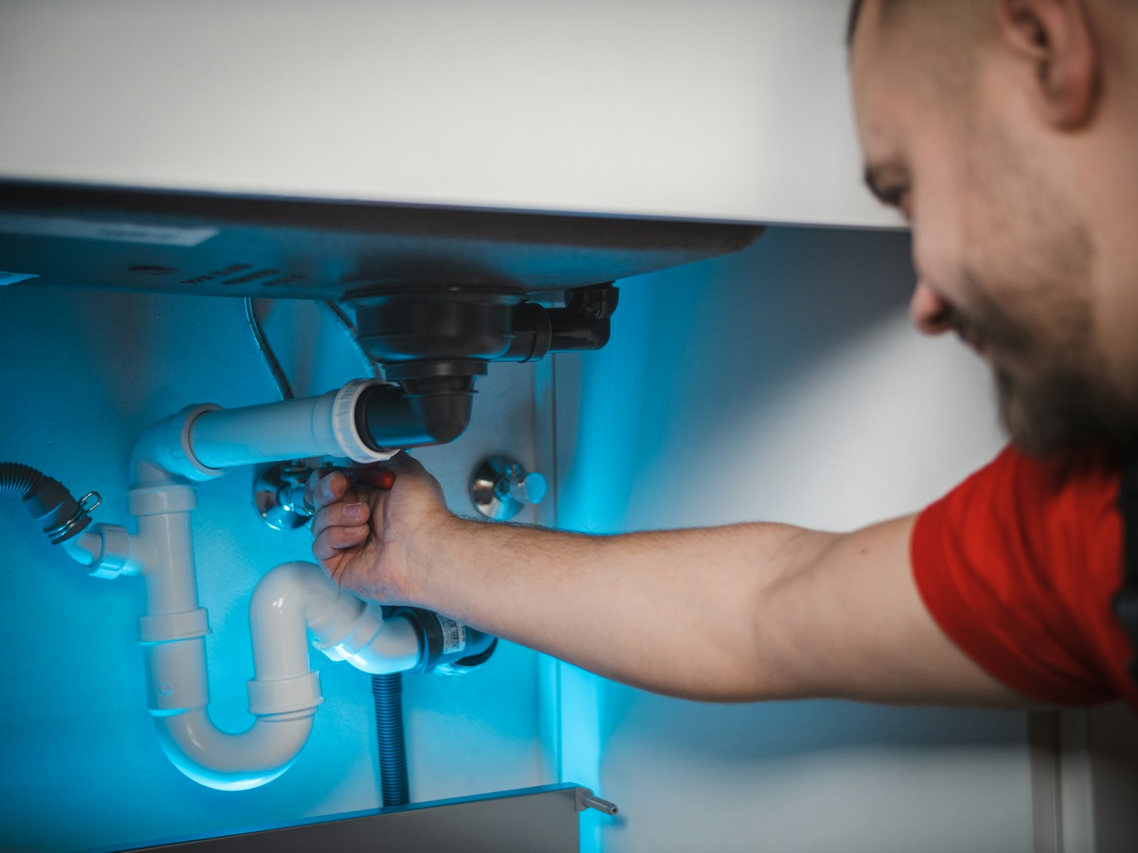 Instalator care strânge racordurile sifonului de sub o chiuvetă